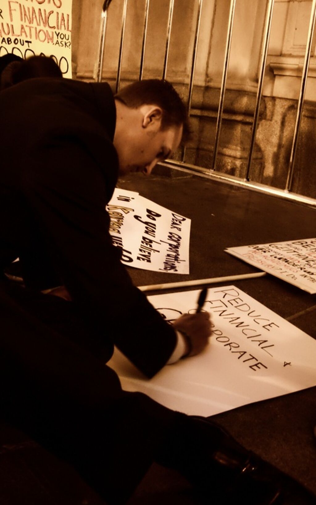 a protestor makes a sign while crouching on the ground