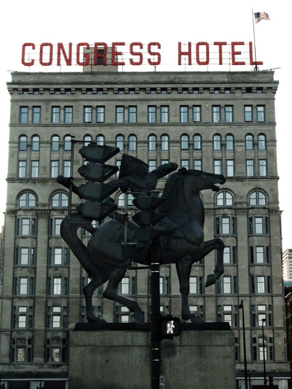 a road signal reads WALK in front of a statue of a horse rider in front of the Congress Hotel